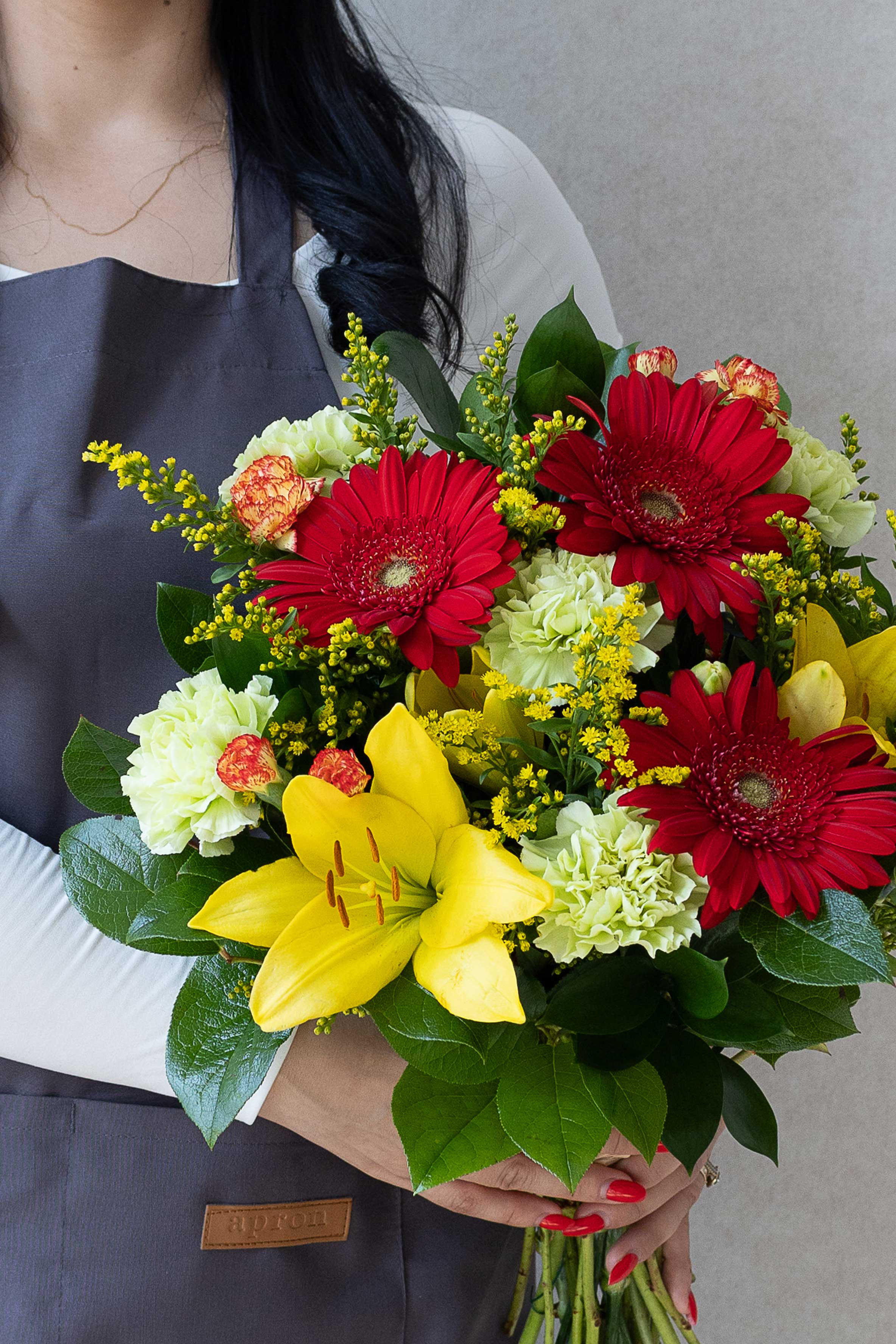 Colourful bouquet with red gerberas, yellow lily, and seasonal foliage.