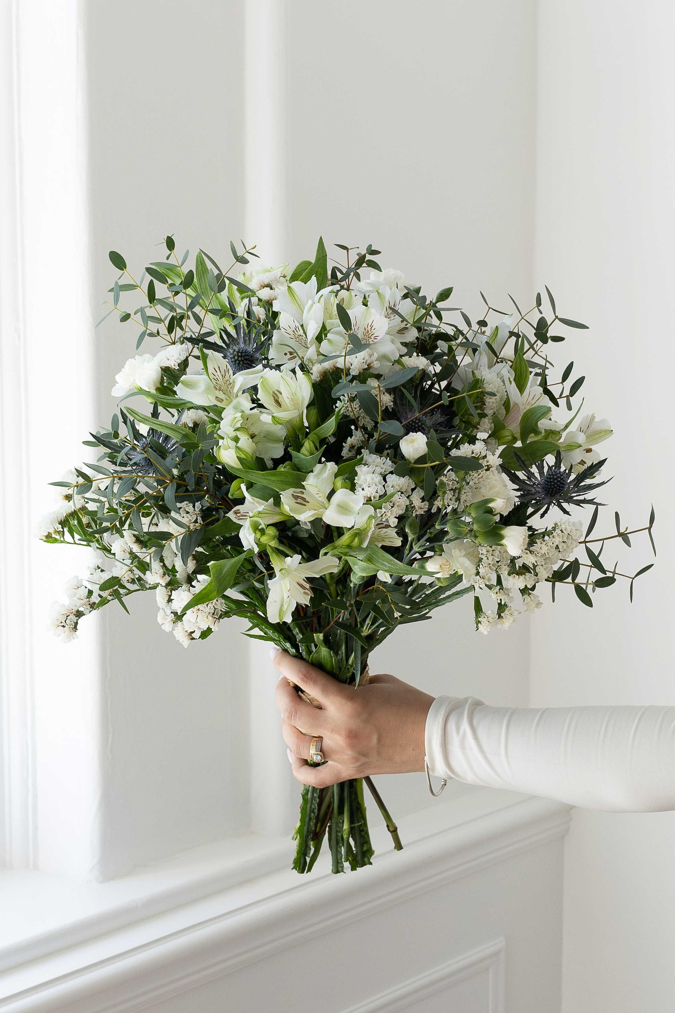 White floral bouquet with eucalyptus and blue thistles.