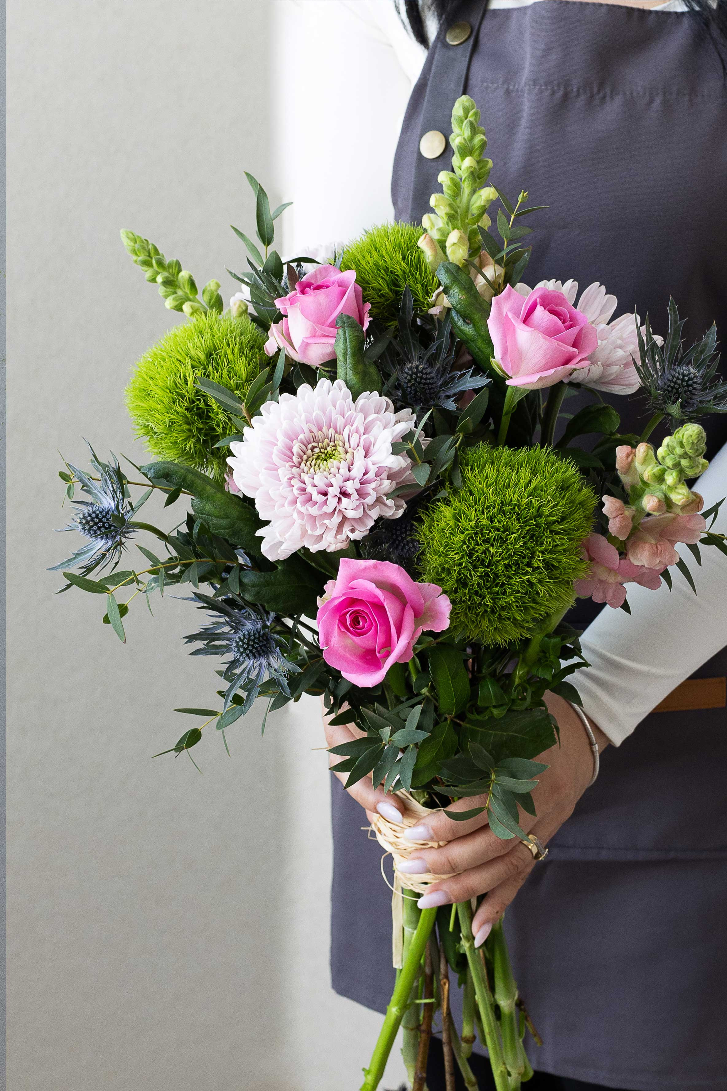 Pink roses and green dianthus bouquet with blue thistles.