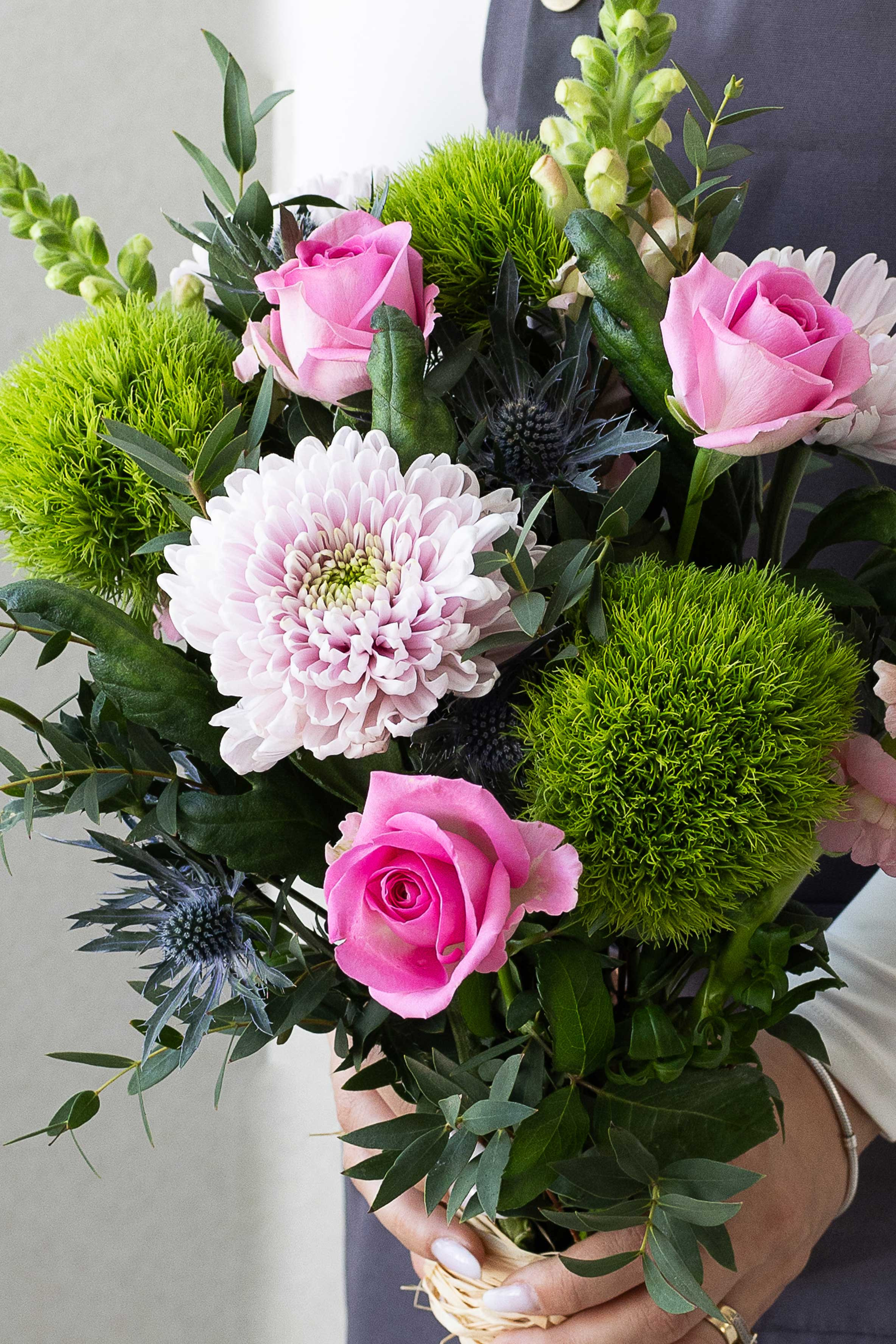 Close-up of pink roses, green dianthus, and blue thistles.
