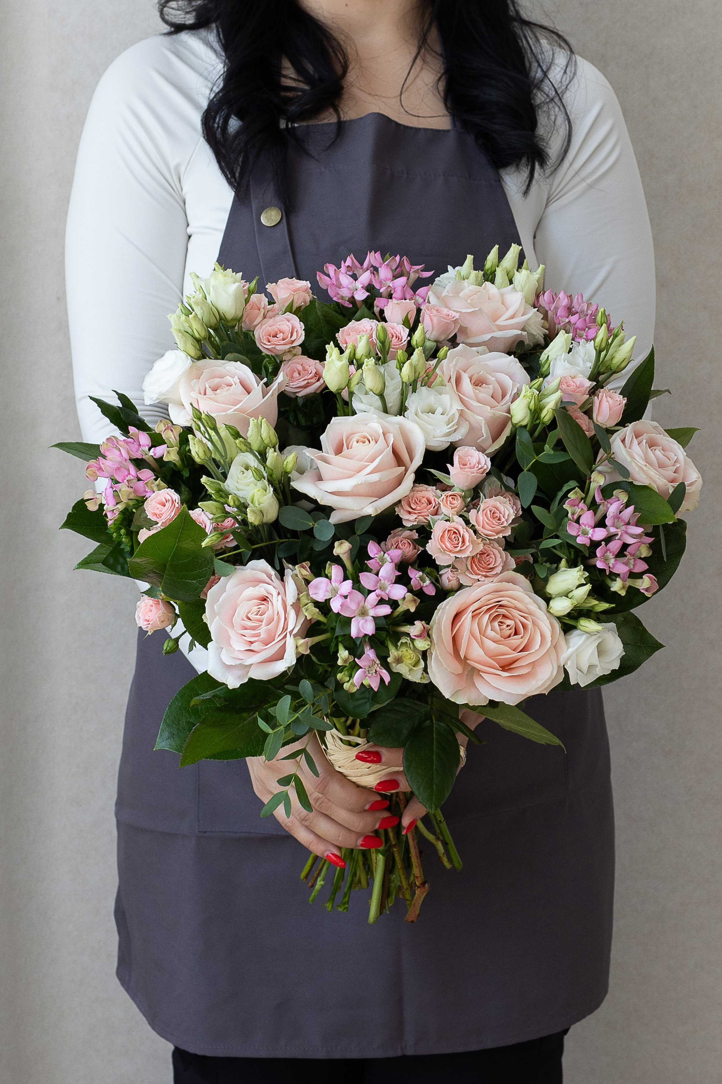 Florist holding a pastel bouquet of pink roses and white flowers.