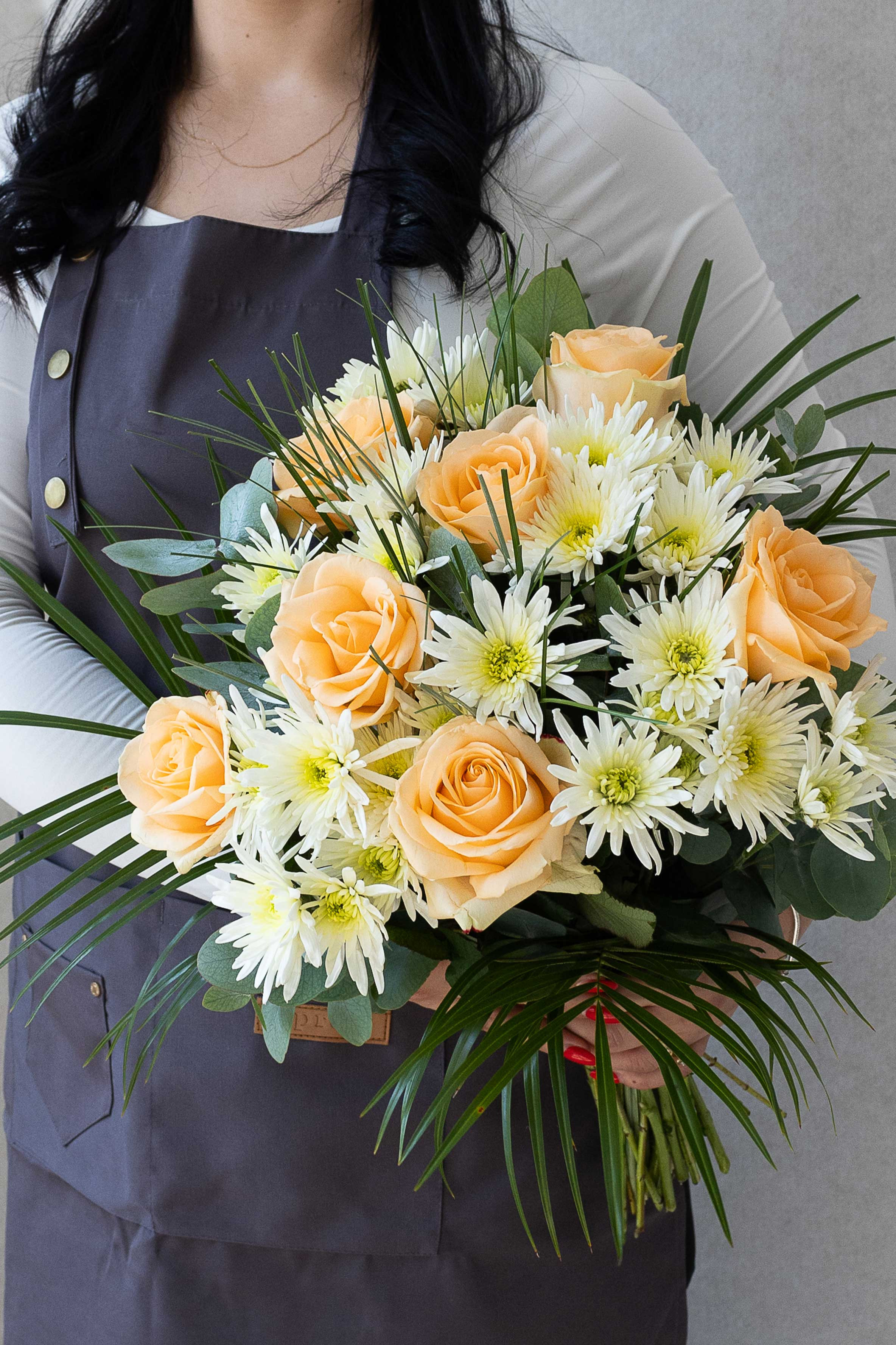 Florist holding a peach rose and white chrysanthemum bouquet.