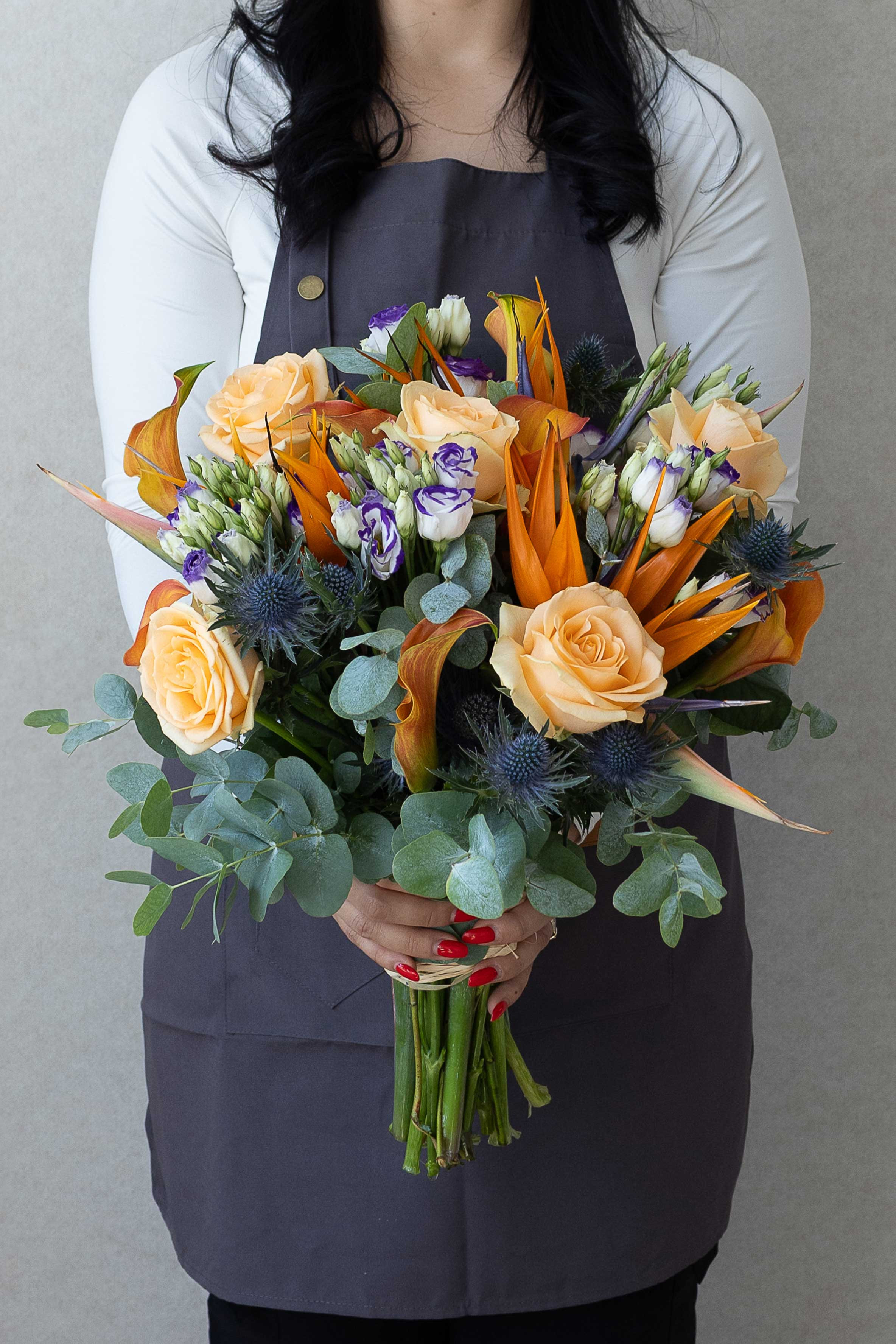 Florist holding a bouquet of peach roses, bird of paradise, lisianthus, thistles, and eucalyptus.
