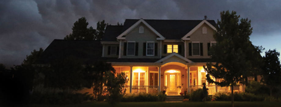 The Best Natural Gas Whole House Generator House Below a Stormy Sky with Upstairs and Downstairs Lights.