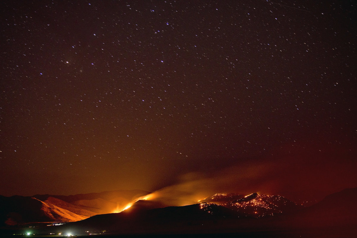 A wildfire pushed by warm, dry winds climbs a hillside as the wind carries sparks and ash to ignite more fires in its path. and threaten a community.