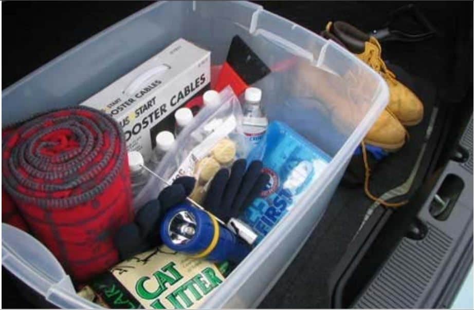 A Winter Emergency Car Kit packed in a plastic bin, ready to load into a trunk. Boots and shovel next to bin.