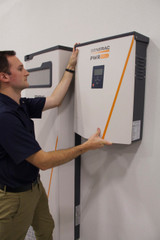 An installer mounts a PWRcell 11.4kW Inverter next to Generac PWRcell Battery Cabinet.