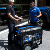 Two Men Examine the DuroMax XP15000HXT 15000 Watt Generator on a Paver Patio with Iron Pipe Railing and Pickup Trucks in the Background