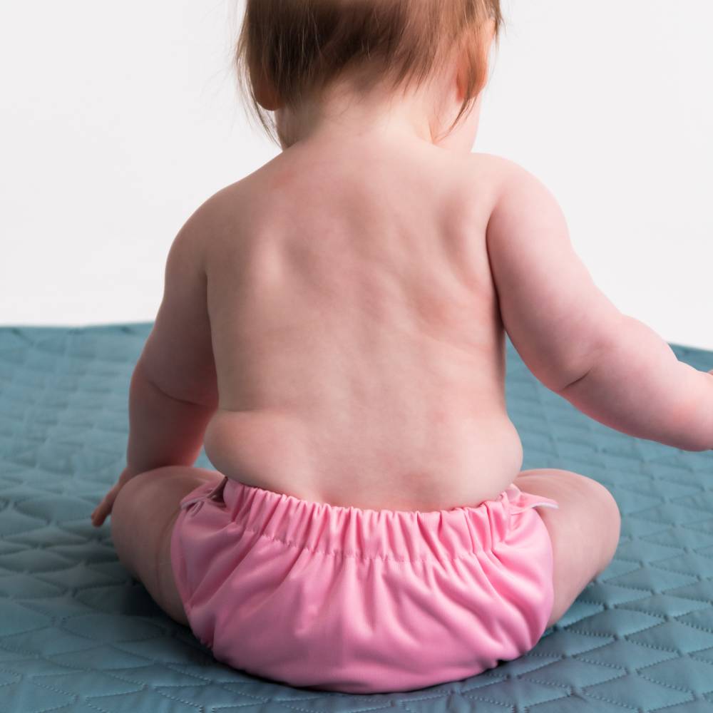 baby sitting up with pink swim nappy on