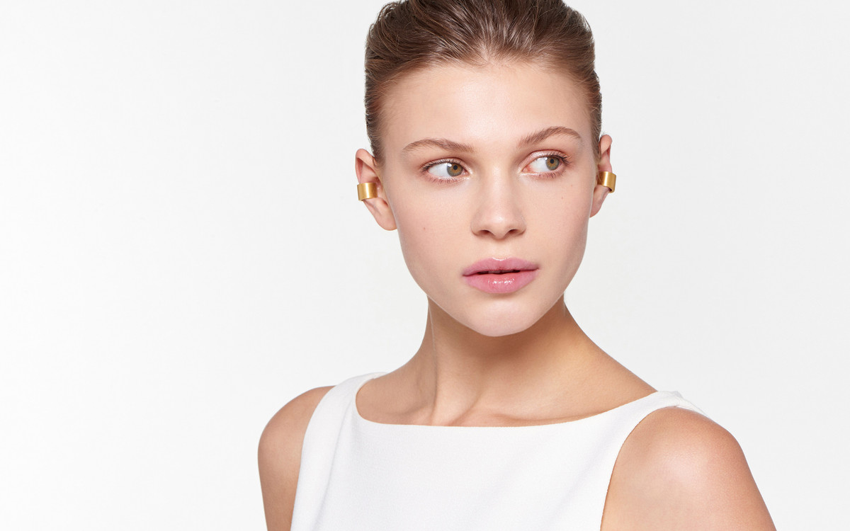 lovely female model glancing sideways wearing vibrant 22 karat gold ear cuffs in satin finish