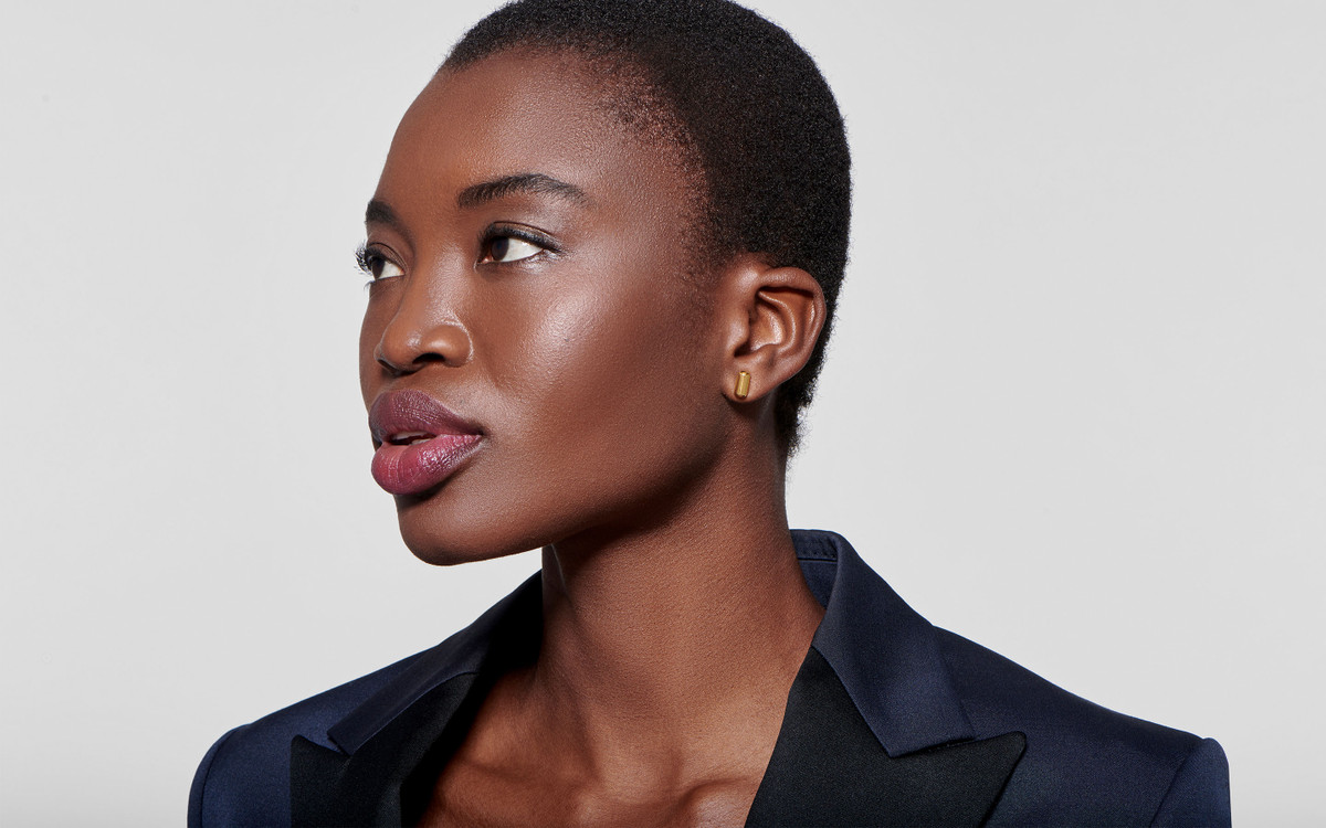 graceful black model looking pensively to the side with linear 18 karat polished gold earrings molded into barrels