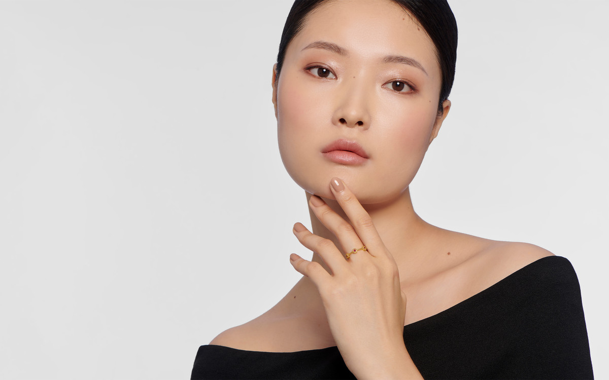 Female model wearing 22 karat gold ring with gemstones.