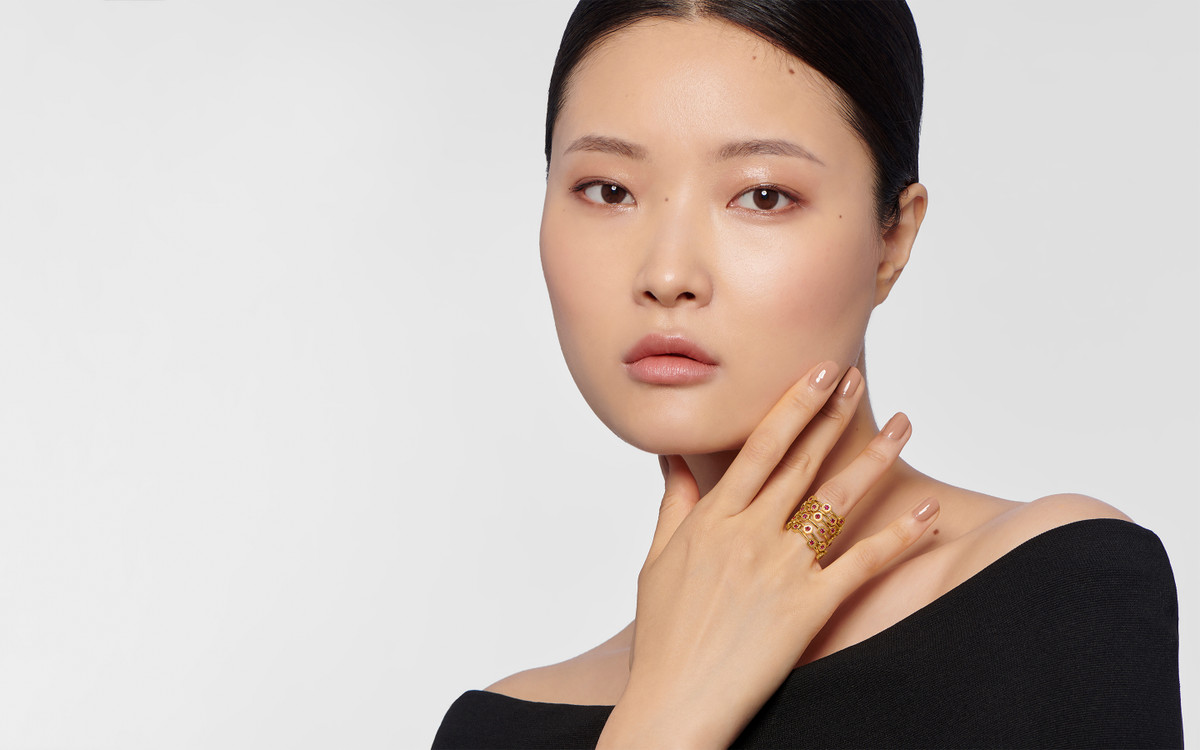 Female model wearing 22 karat gold ring with gemstones.