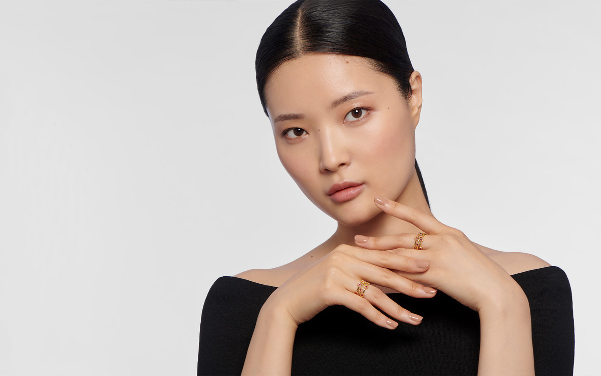 Female model wearing 22 karat gold ring with gemstones.