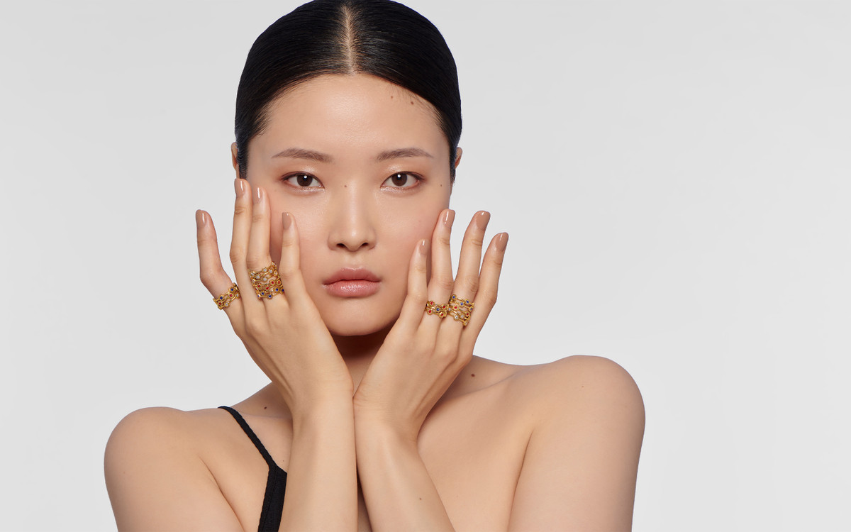 Female model wearing 22 karat gold ring with gemstones.