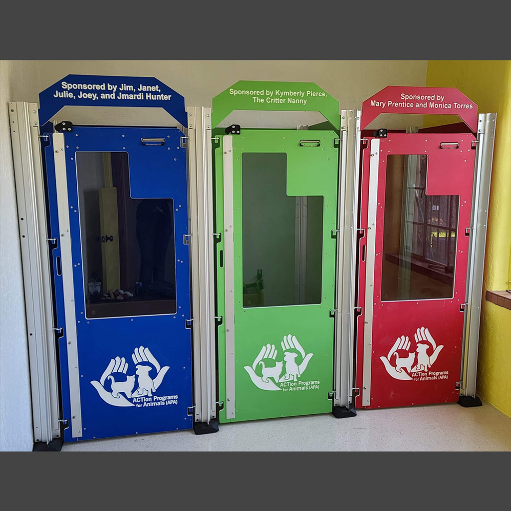Row of 3 free standing kennels in royal blue, lime green and red. The custom logo on the half glass doors makes it feel more personalized to their location. The solid bottom portion of the doors allows the more timid dogs to duck behind and feel safe while still leaving great visualization into the kennel through the top glass portion. The headers above the doors shows who has sponsored each kennel.  