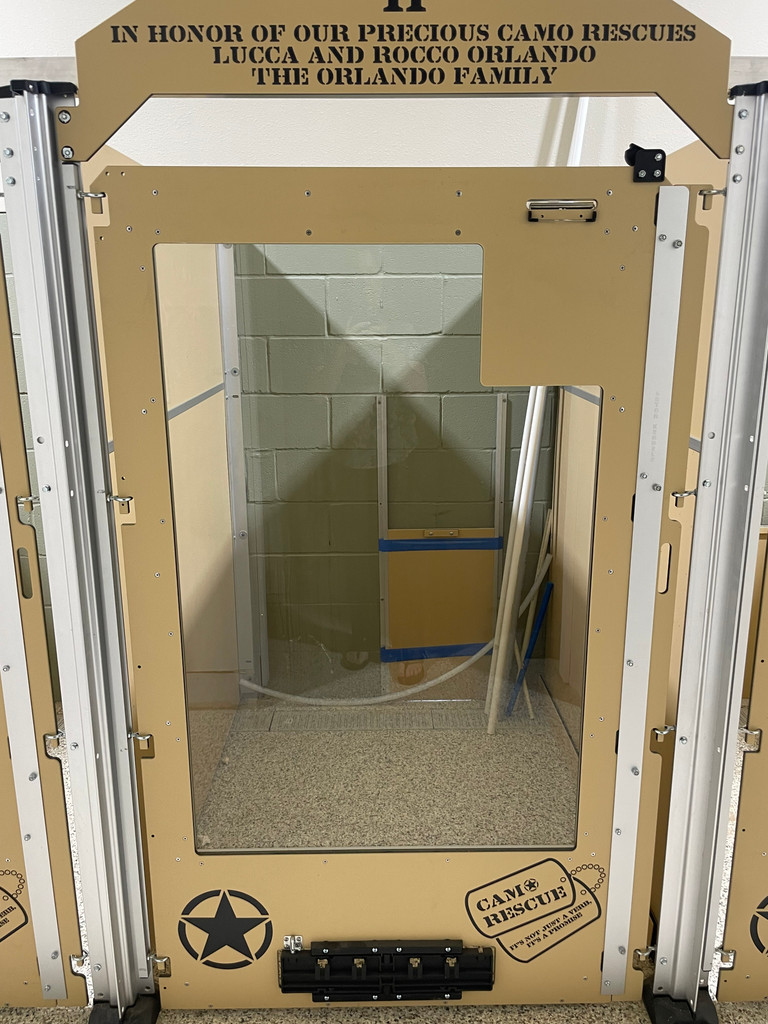 Our tan and black kennels with the custom logo. Our kennel doors and gates come standard with a headers, and clipboard and then the customer wanted donor information added to the headers and chose to purchase our fast feeder systems. The assembly of the transfer door is still pending in this picture and waiting for the hole to be added to the exterior wall. 