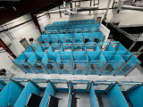 View from above a couple rows of dog kennels. This image allows you to see inside some of the kennels and how the kennels are arranged. The rows of kennels are layed out back-to-back with aisles in between.