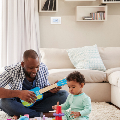 Father and son playing on the living room floor with the Sensi thermostat on the wall in the background