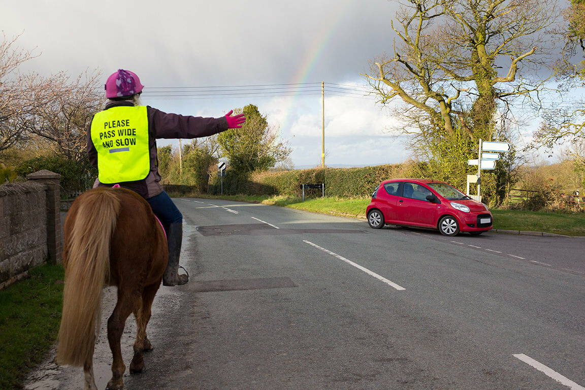 Safety tips when out hacking Horse rider in hi-vis on road arm signalling to turn