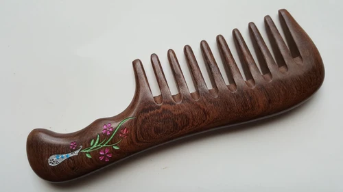 A dark brown wooden comb with a floral vase design on the handle. The flowers are pink, green, and white