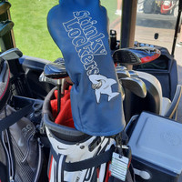 Stinky Lockers Personalized Golf Luggage Tag with Loop-OTO, blue leather golf club head cover with embroidered shark logo and text, attached to golf bag on a golf cart.