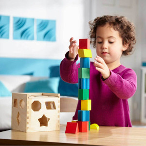 Child building colourful wooden block tower with Melissa & Doug shape sorting cube toy on table