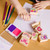 Melissa & Doug Friendship Stamp Set - child stamping designs onto light purple paper with 2-colour inkpad, pencils and completed artwork visible | Peekaboobaby