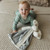 Infant holding Bunnies By The Bay Grey Buddy Blanket Lovey - lifestyle shot showing baby with grey blanket and attached bunny toy