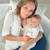 Mother holding newborn baby while dark navy Theraline Plushy Moon nursing pillow supports breastfeeding