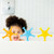 Toddler in foam bath surrounded by blue, orange and yellow Ubbi starfish toys