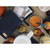 Overhead view of dark blue pouch beside apples, bowl with food, white dishes, and meal storage containers.