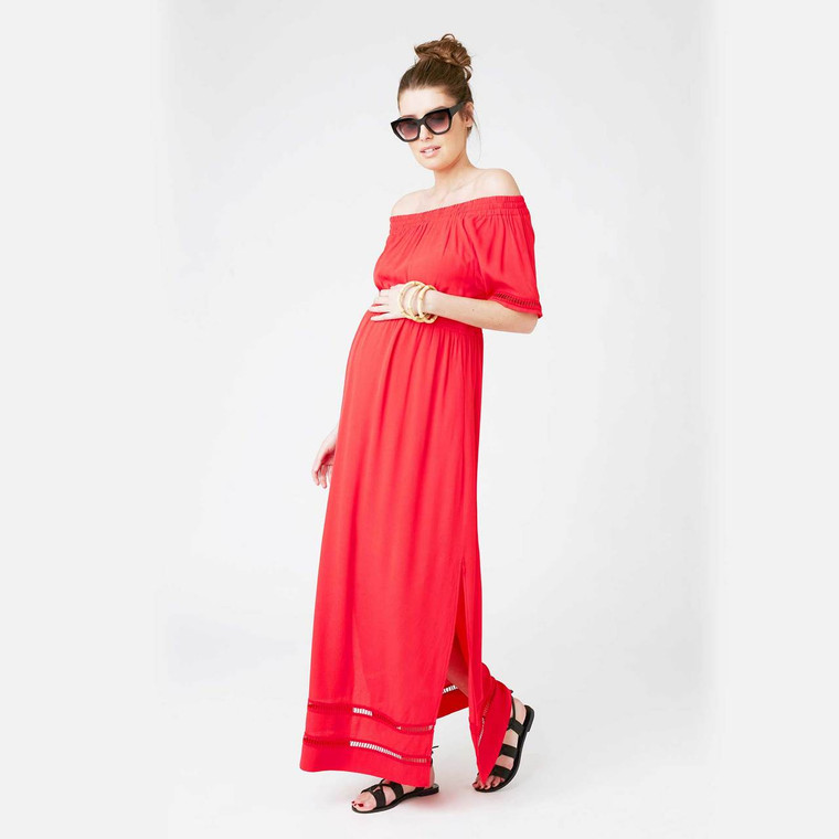 Pregnant woman wearing Ripe Maternity coral red off-shoulder maxi dress with sunglasses and black sandals on white background