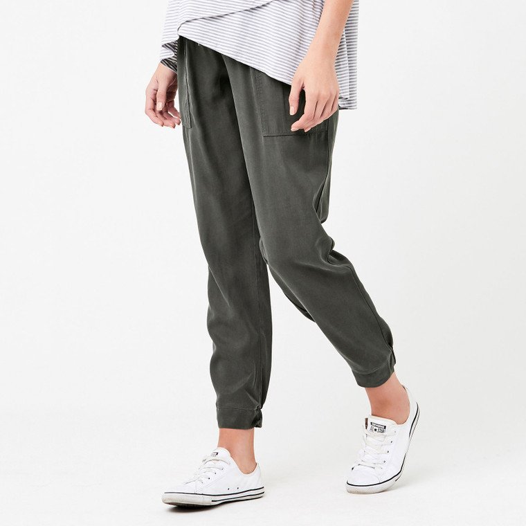 Pregnant woman wearing olive green Tencel jogger pants with elasticated cuffs, striped top and white sneakers