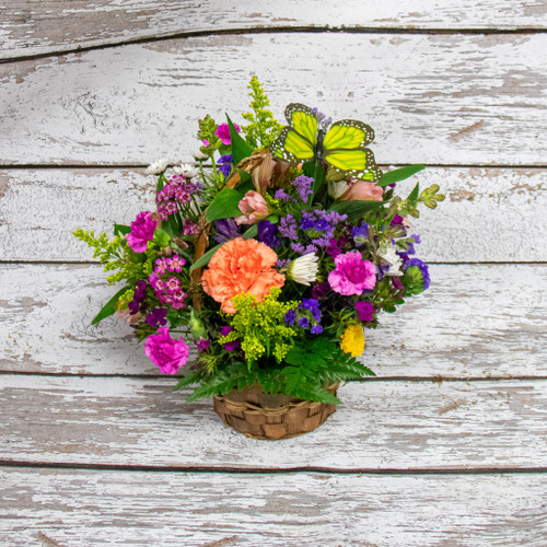 A wicker basket filled with bright colored long-lasting flowers like daisies, carnations, alstromeria and dianthus.