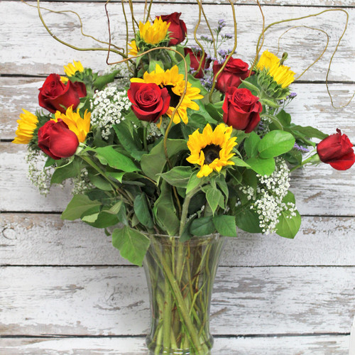 Sunflowers and red roses with tall curly willow in a large clear glass vase