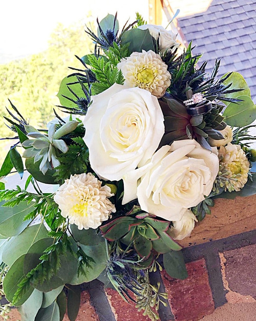 This gorgeous free style bouquet is designed with succulents, white roses, white mums, mixed greens, thistle, and eucalyptus! An amazing mix of soft whites and all greens!