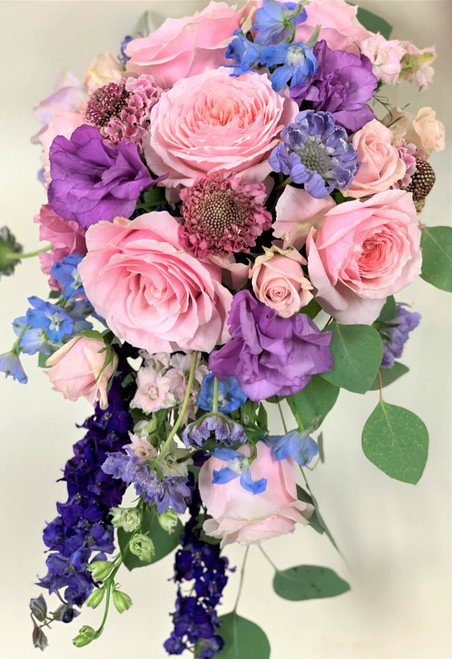 A beautiful cascading bouquet of Pink Roses, Lisianthis, larkspur and mixed flowers make up this colorful bridal bouquet!