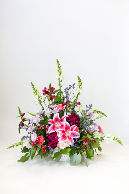 The Graceful Lady Sympathy Tribute is a one-sided arrangement with locally grown stargazer lilies. This basket arrangement is a classic pink display with other pink and purple accent colors.