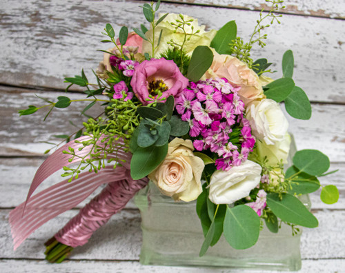 This gorgeous bouquet is designed with pastel roses with pops of purple and set with greenery.