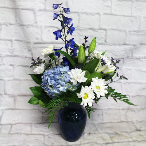 A blend of blue and white flowers including hydrangea, roses, lilies and other garden flowers. A great choice for a sympathy arrangement to the home or the service.