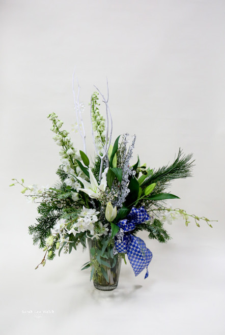 A vase arrangement with lilies, greenery, and silver accents