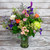 Large arrangement of wildflowers, roses, lisianthus, larkspur, and spider mums with mixed greenery in a clear glass vase