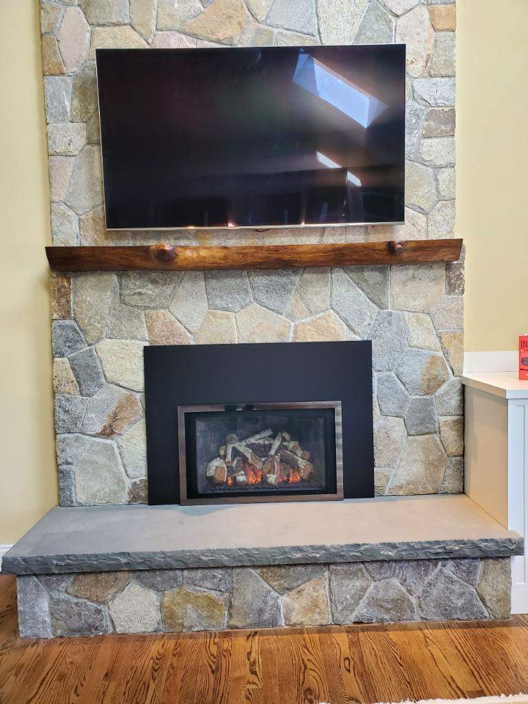 Another Fireplace Insider gas insert installation showing the proper stack: insert at the bottom, combustible wood mantel respecting the manufacturer's clearance, and a TV mounted at a comfortable viewing height above.