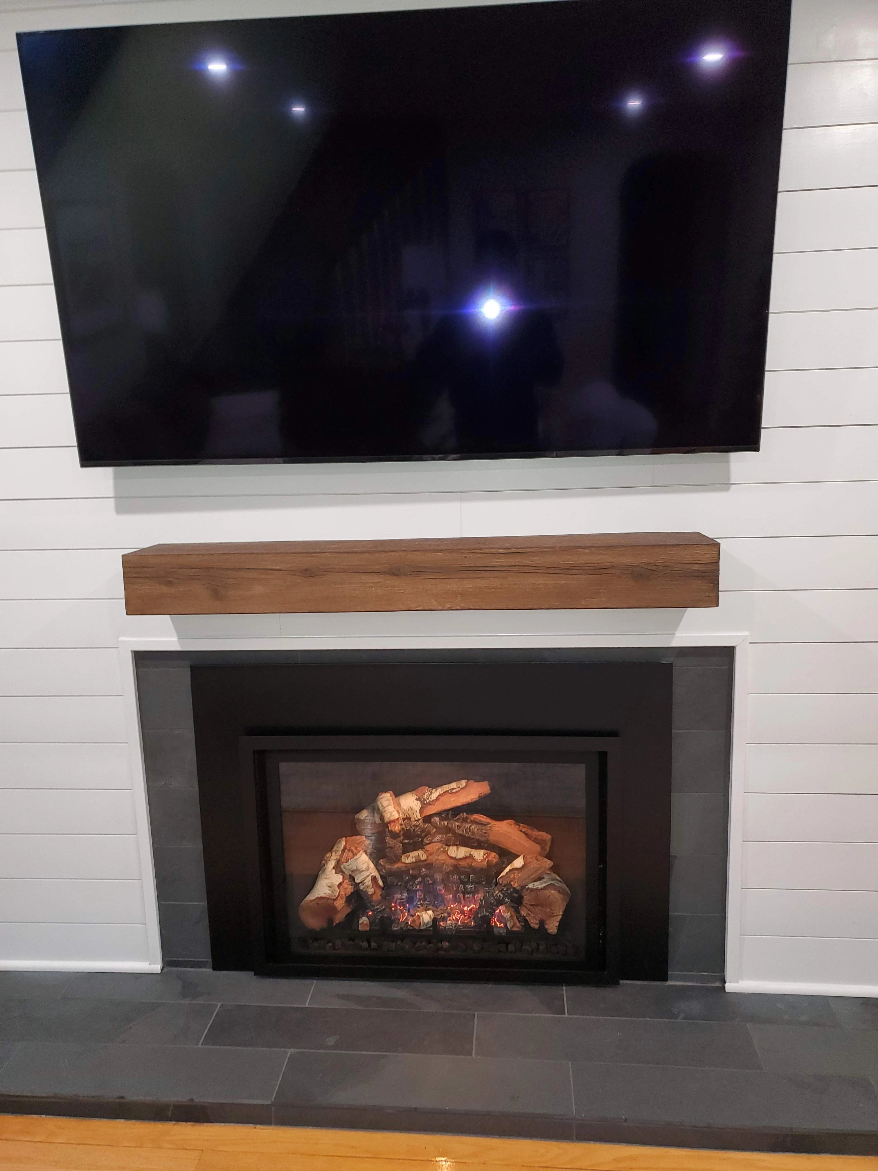A gas fireplace insert installation completed by Fireplace Insider, with a TV mounted above a wood mantel that respects the manufacturer's clearance to combustibles.