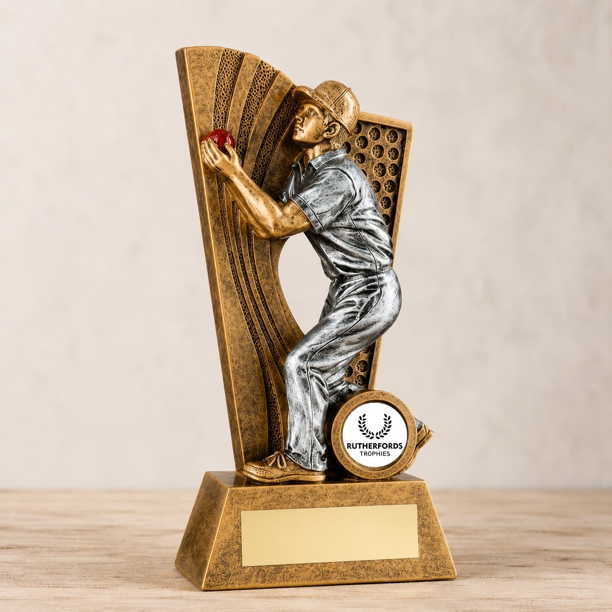 Antique gold and silver cricket fielder trophy holding a red cricket ball with an engraving plate