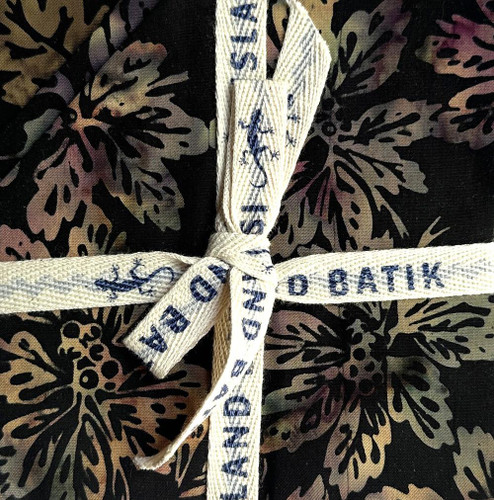 Lumin Fabrics Island Batik Woodland Warmth Batiks 5 Inch Squares, tied with a cream-colored fabric ribbon that has blue printed text.