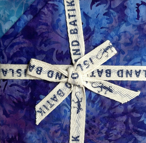 Lumin Fabrics Island Batik Springtime Bouquet Batiks 5 Inch Squares, colorful fabric with floral pattern wrapped with white ribbon with blue text.