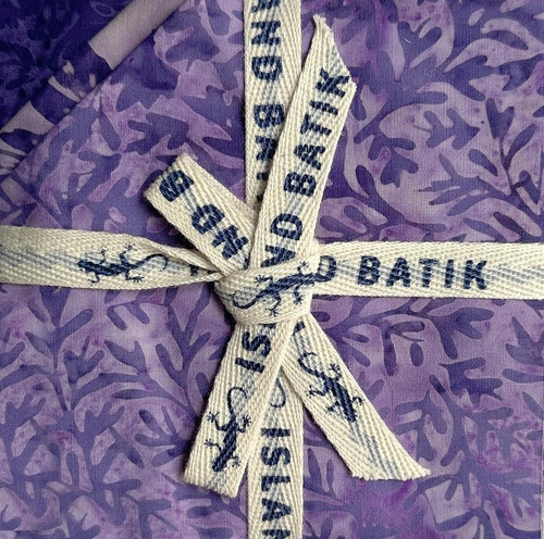 Lumin Fabrics Island Batik Sunflower Spice Batiks 5 Inch Squares, close-up of a tie with the brand name and design, on a purple patterned fabric background.