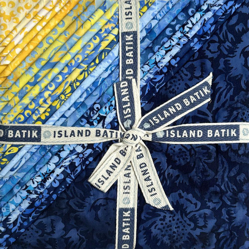 Lumin Fabrics Island Batik Countryside Charm Batiks 10 Inch Squares, a bundle of vibrant blue and yellow batik fabric squares with floral and abstract patterns, tied with a white ribbon labeled 'Island Batik'.